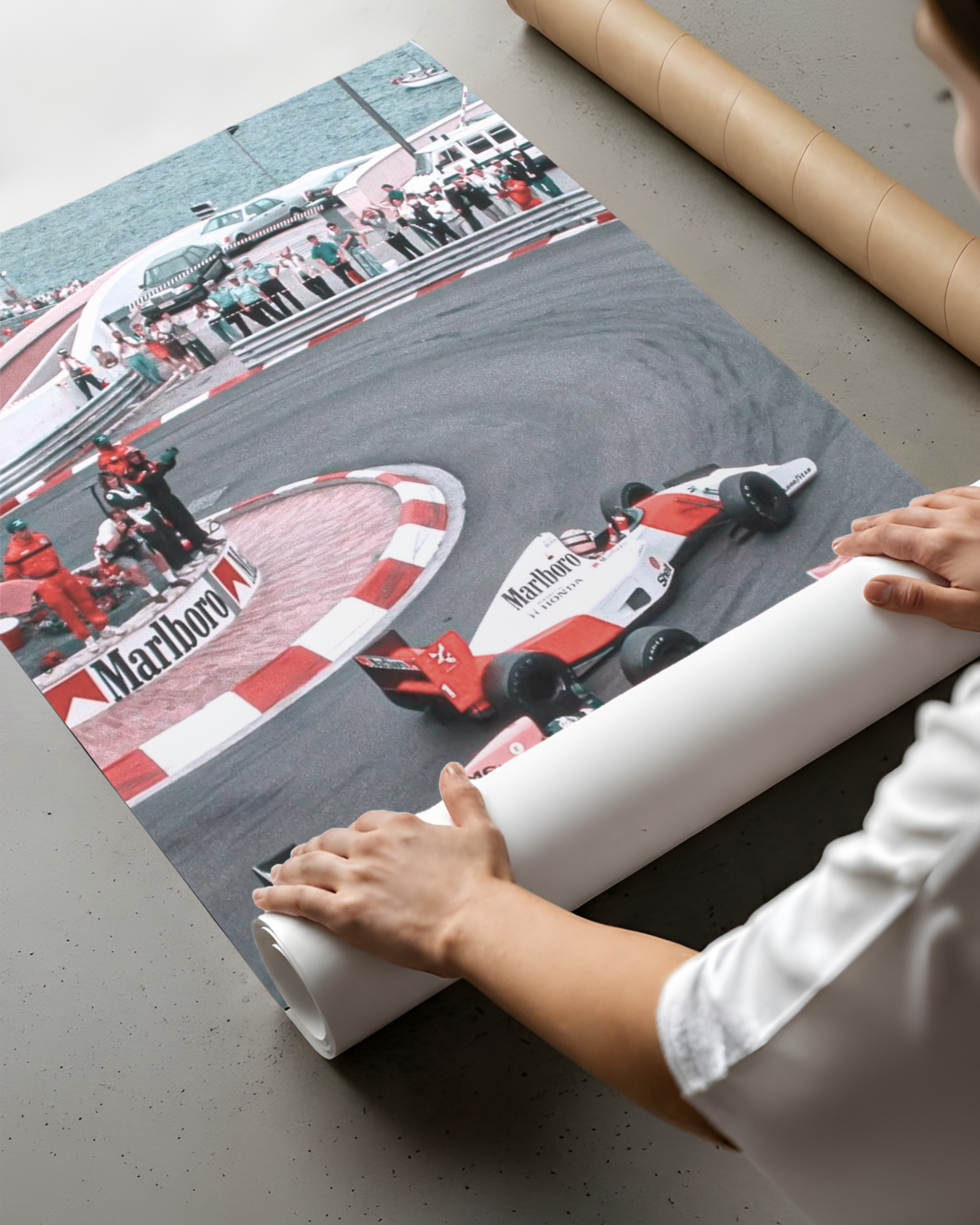 Hands rolling the vintage race-car print into a paper shipping tube on a table.
