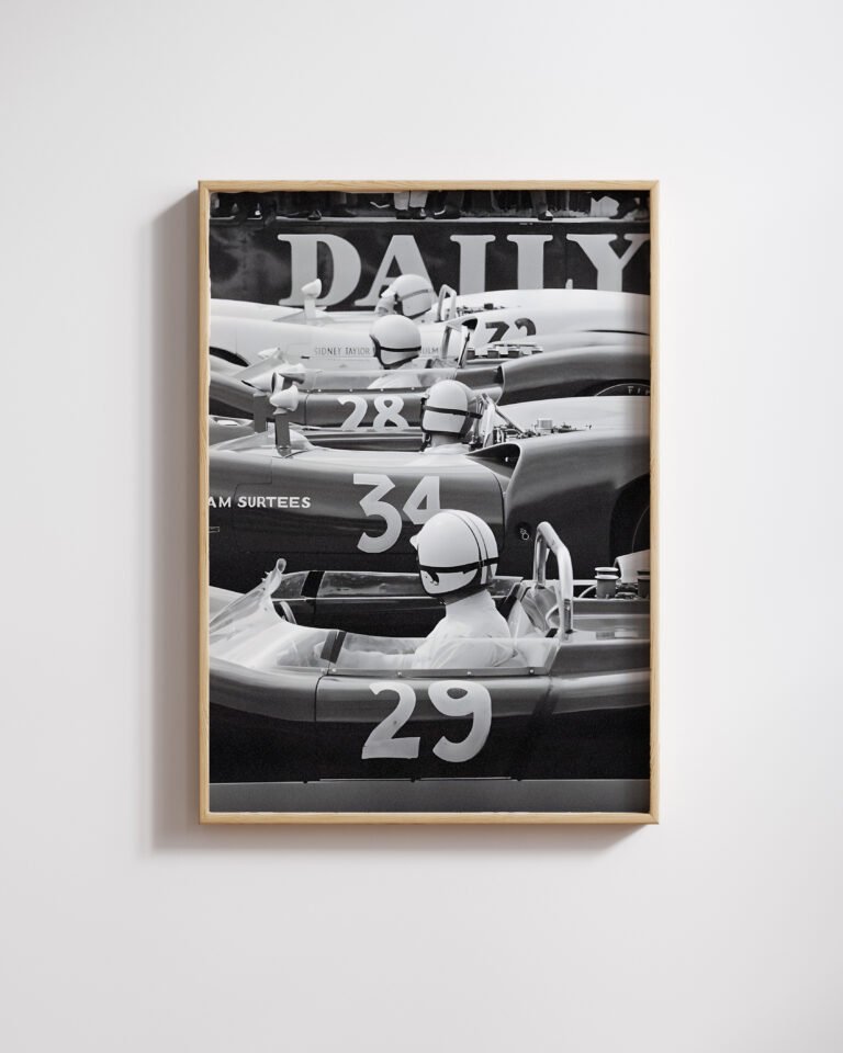 Framed black-and-white photo of vintage open-wheel race cars in a row, drivers wearing white helmets.