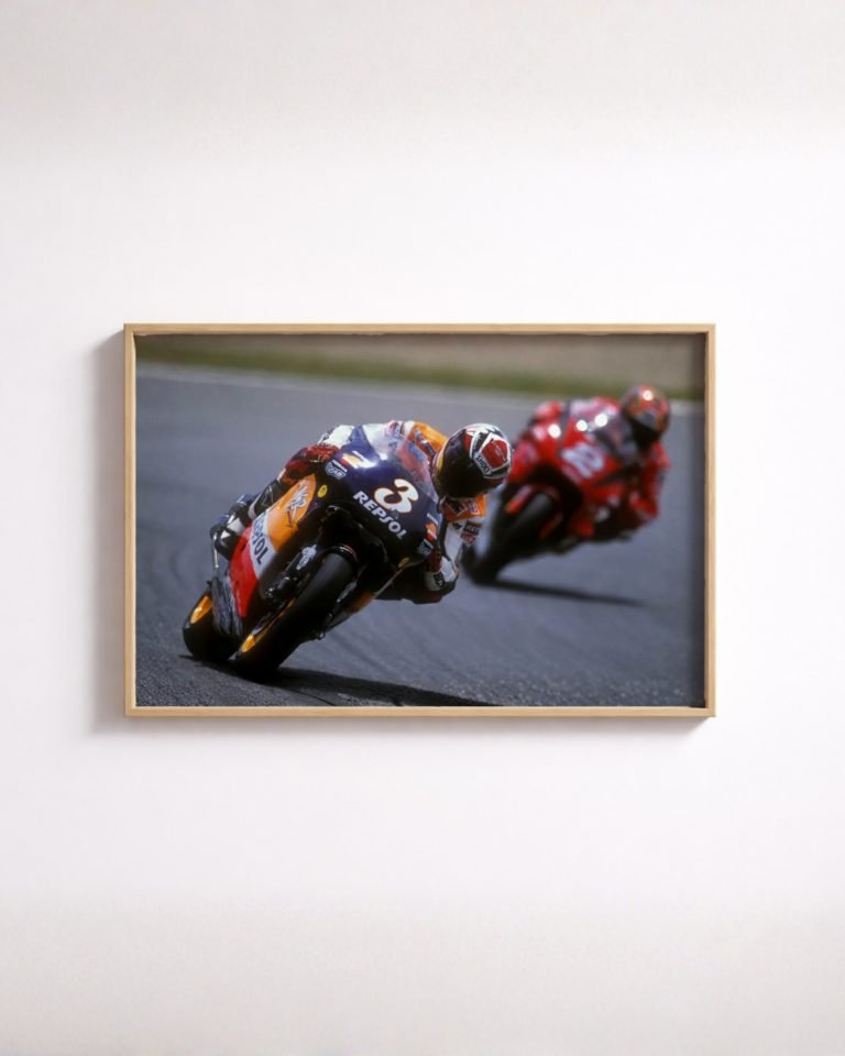 Framed colour photo of a motorcycle racer leaning into a curve ahead of another rider on the track.