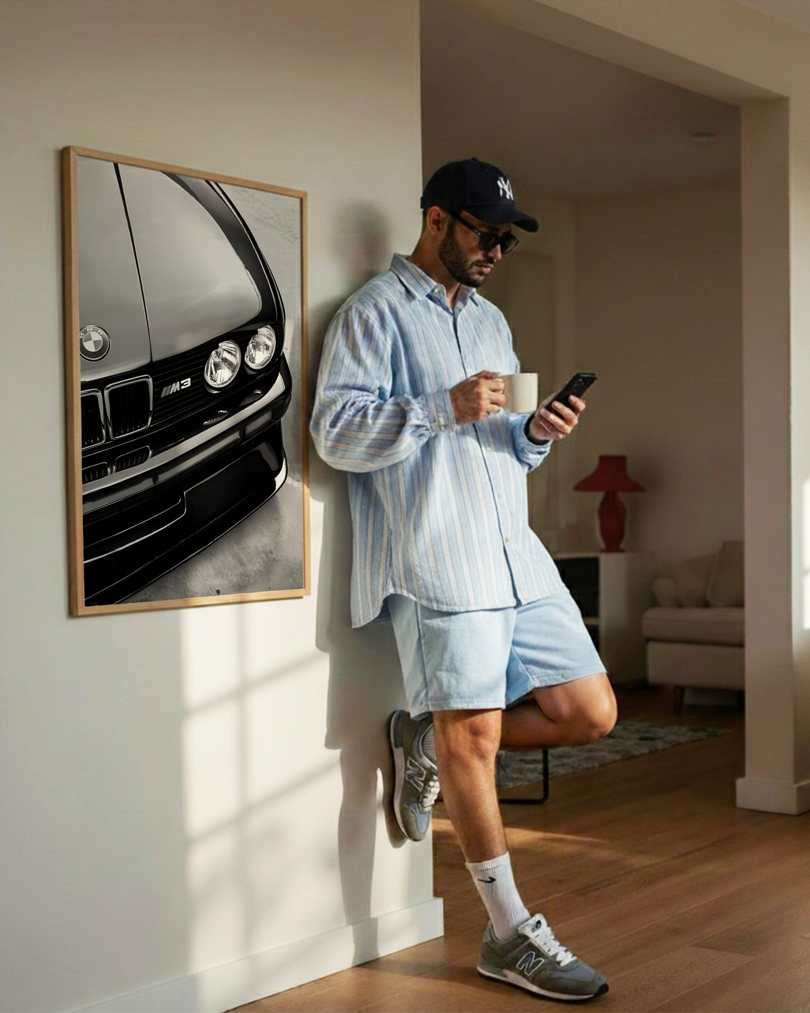 Framed black-and-white BMW M3 print on a hallway wall beside a man checking his phone.