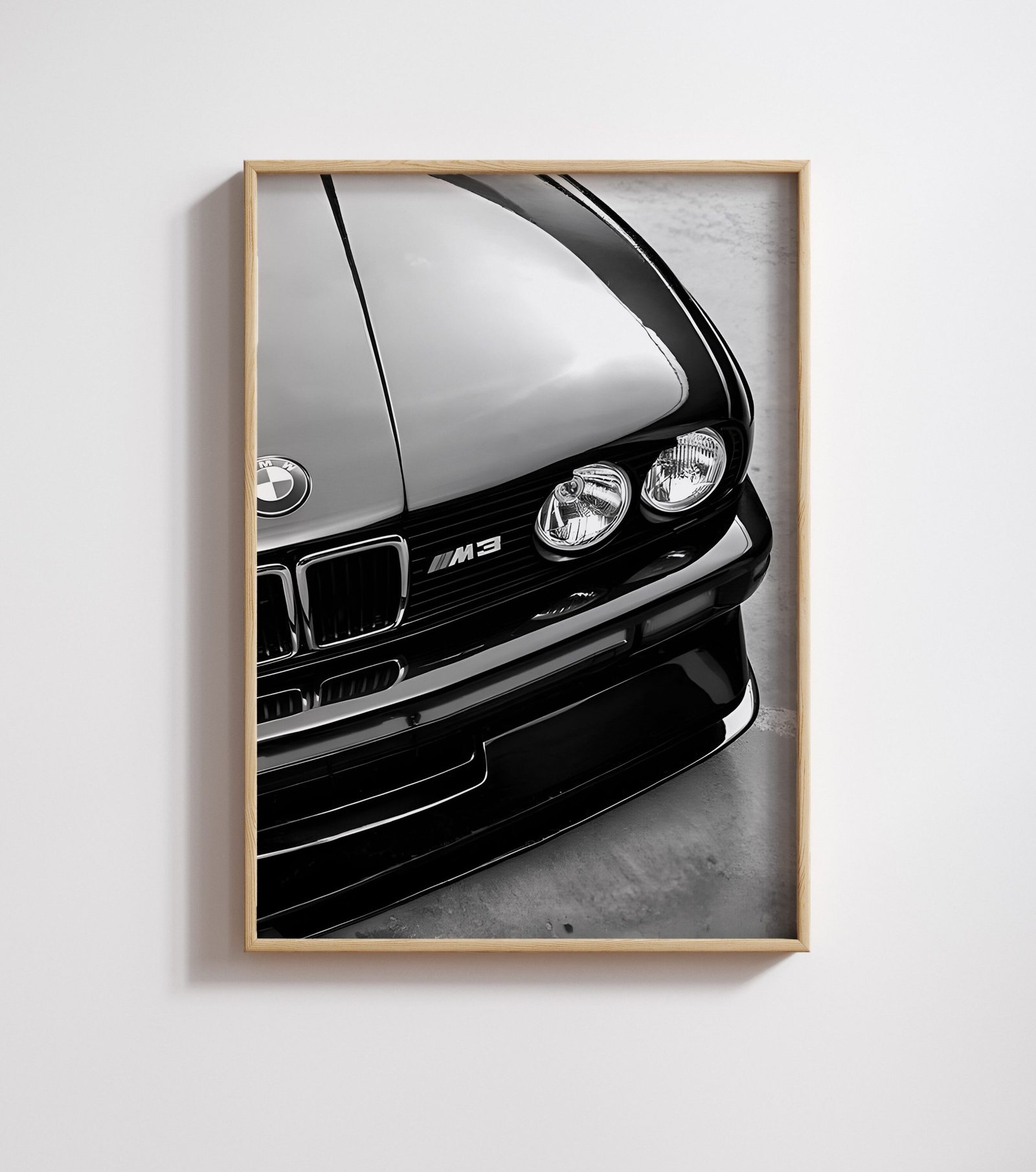 Framed black-and-white close-up of a BMW M3's hood, badge, and headlights on a white wall.