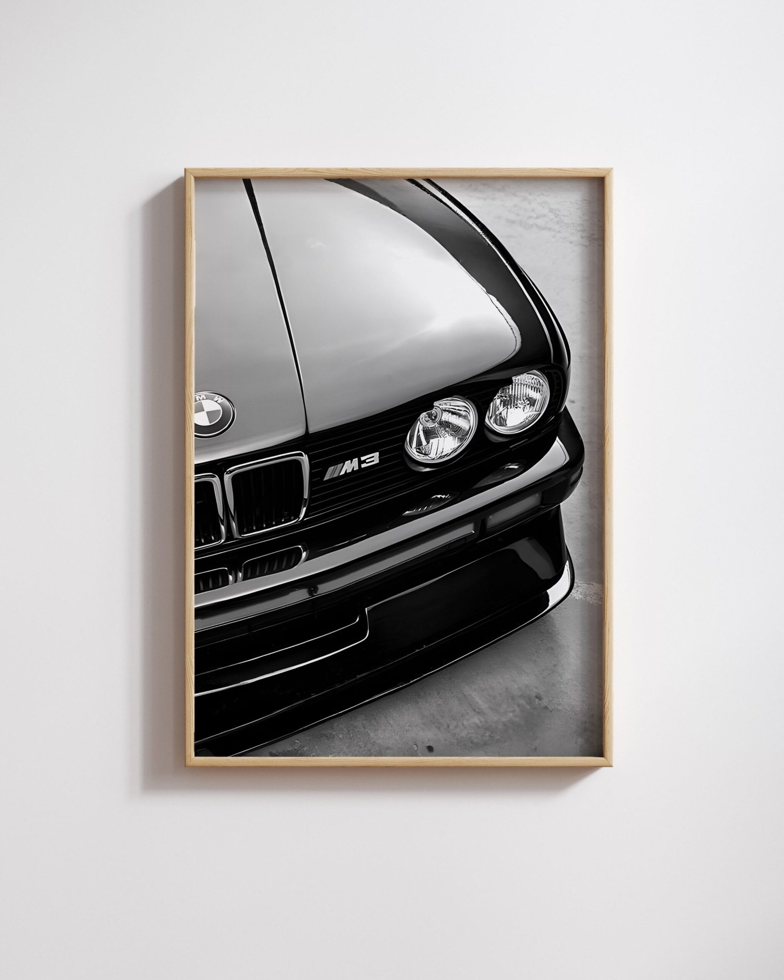 Framed black-and-white close-up of a BMW M3's hood, badge, and headlights on a white wall.