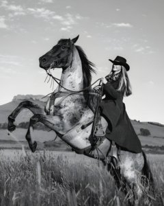 Black and white portrait of a cowgirl riding a horse