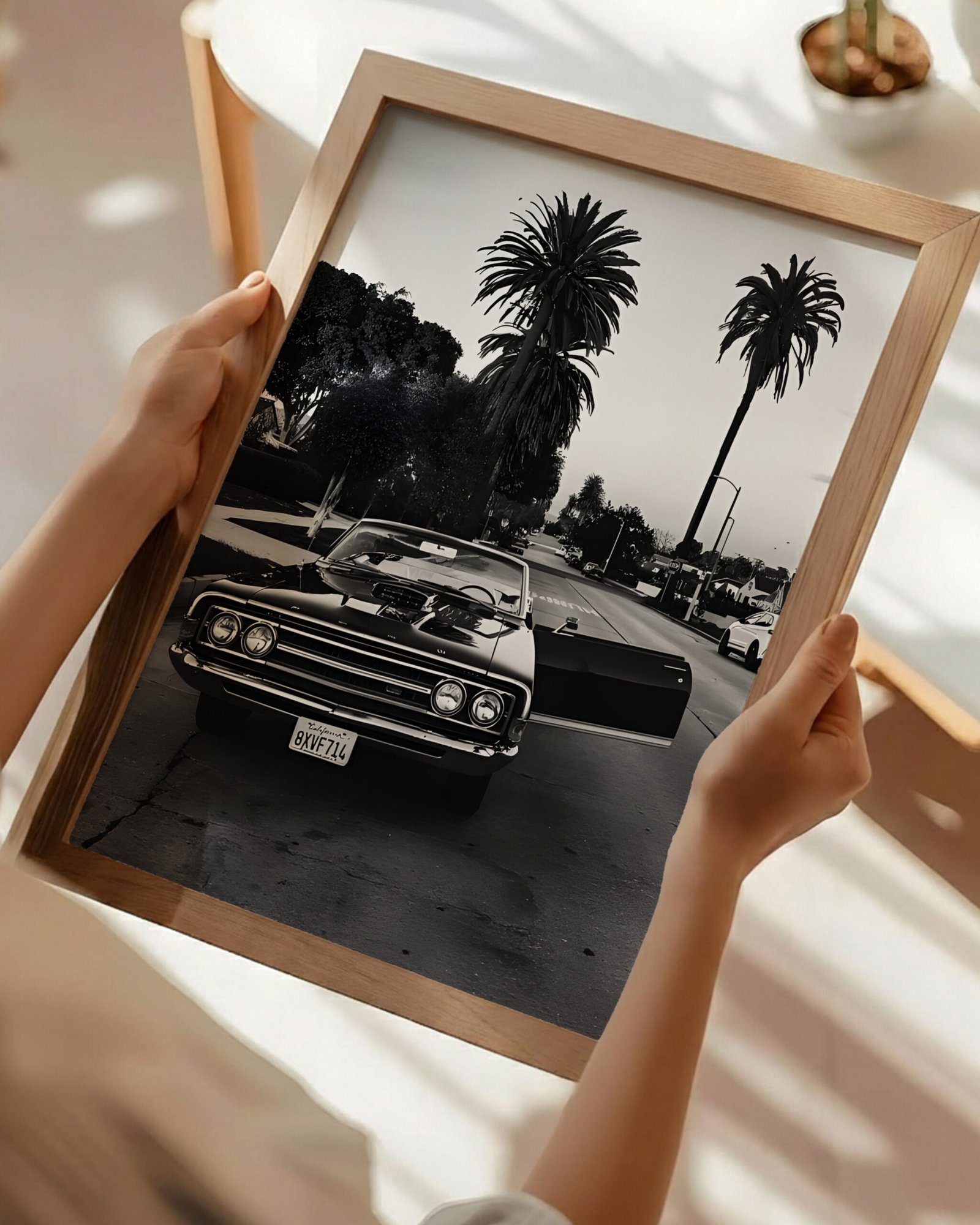 Hands holding a framed black-and-white Impala convertible photo above a café table.