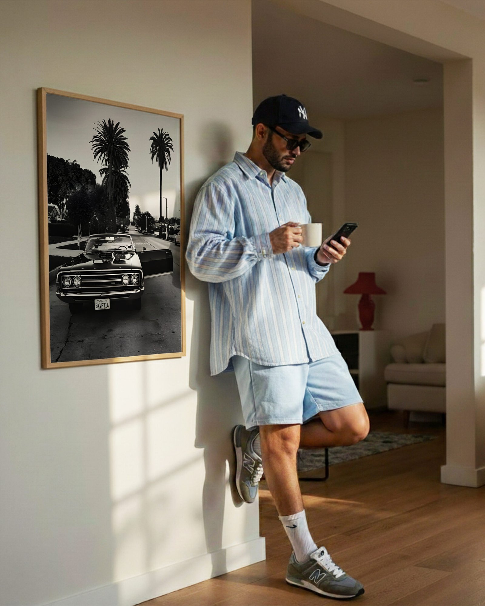 A man leans against a hallway wall beside a framed black-and-white Impala photo, checking his phone.