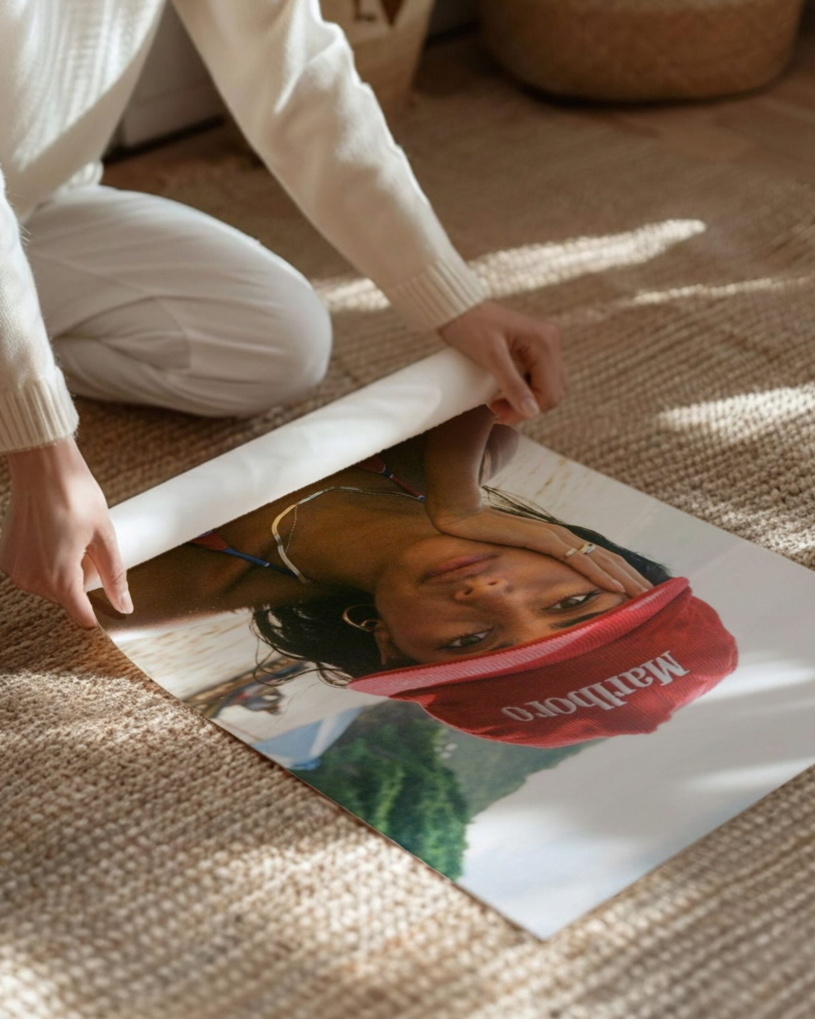 A woman kneels on a woven rug, rolling up the beach portrait poster print.