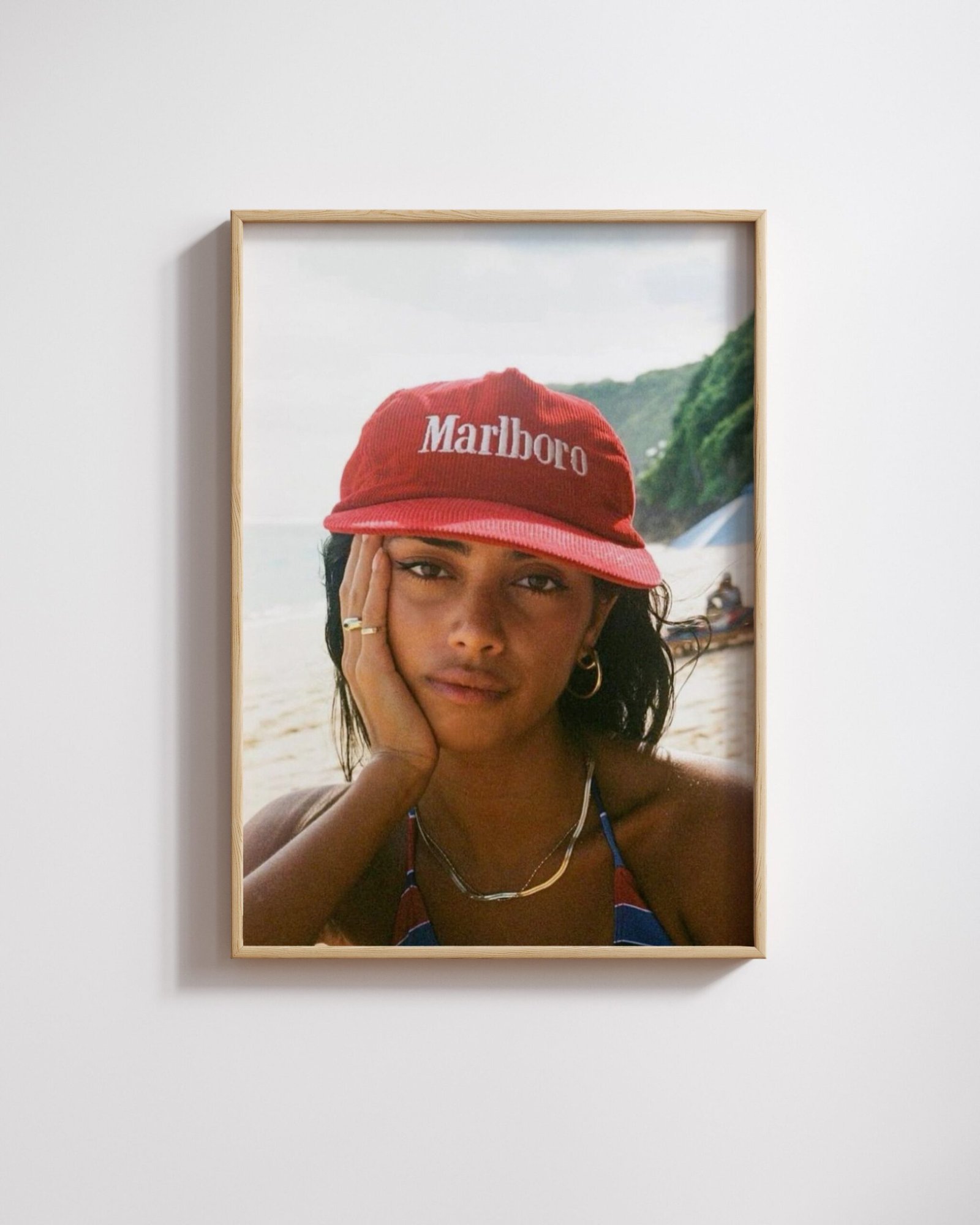 Framed beach portrait of a woman in a red branded corduroy cap, resting her cheek on her hand.