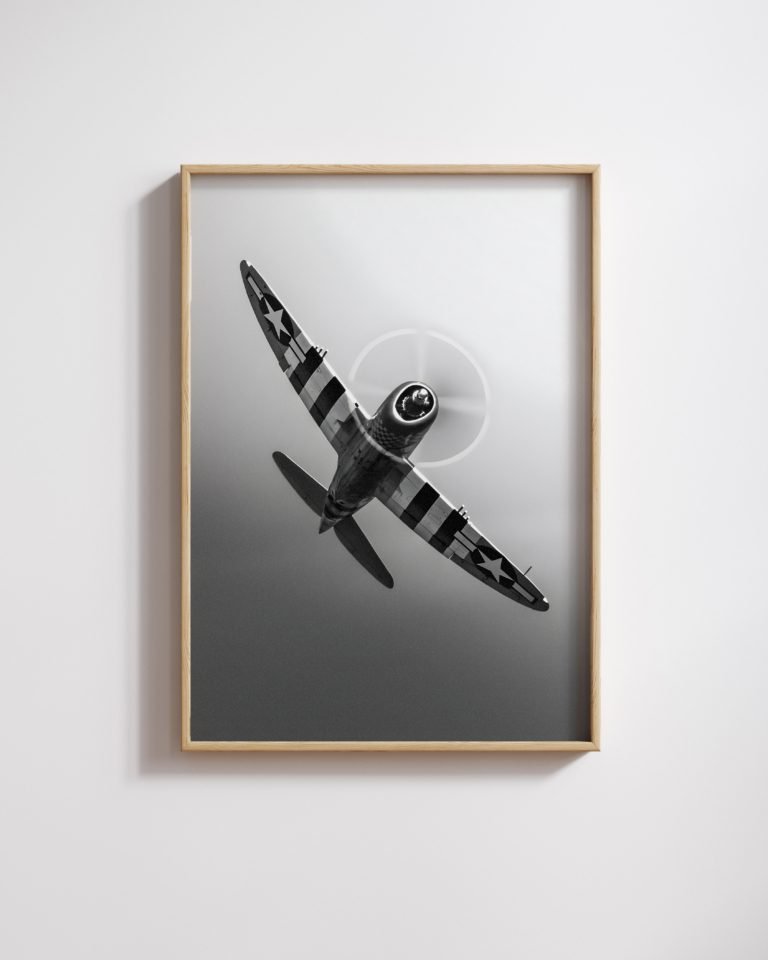 Framed black-and-white photo of a propeller fighter plane banking sharply overhead.
