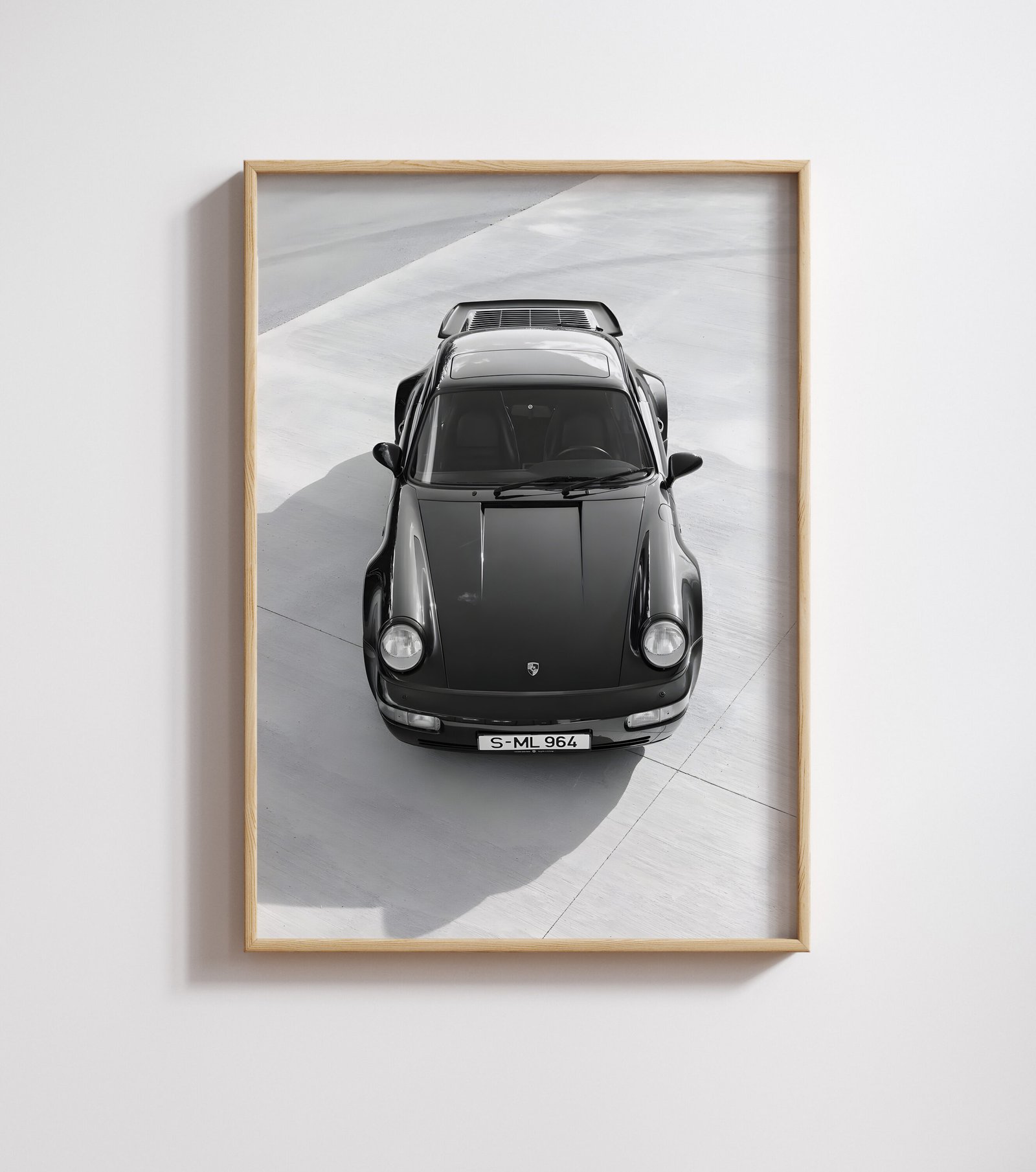 Framed black-and-white print of a black Porsche sports car shot from above, on a plain wall.