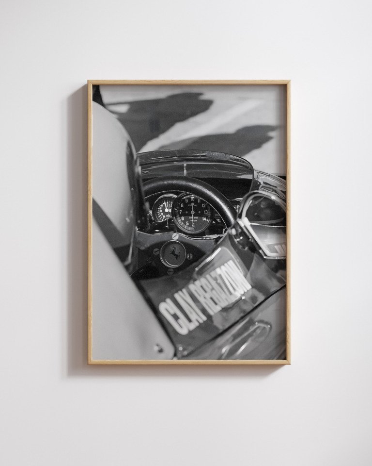 Framed black-and-white close-up of a vintage Formula One cockpit dashboard, steering wheel, and gauges.