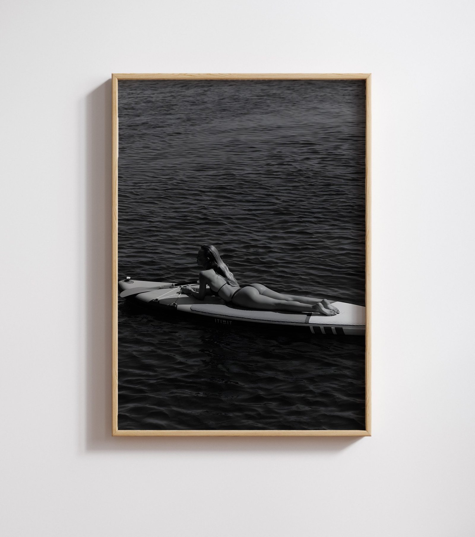 Framed black-and-white photo of a woman lying on a paddleboard on calm, dark water.