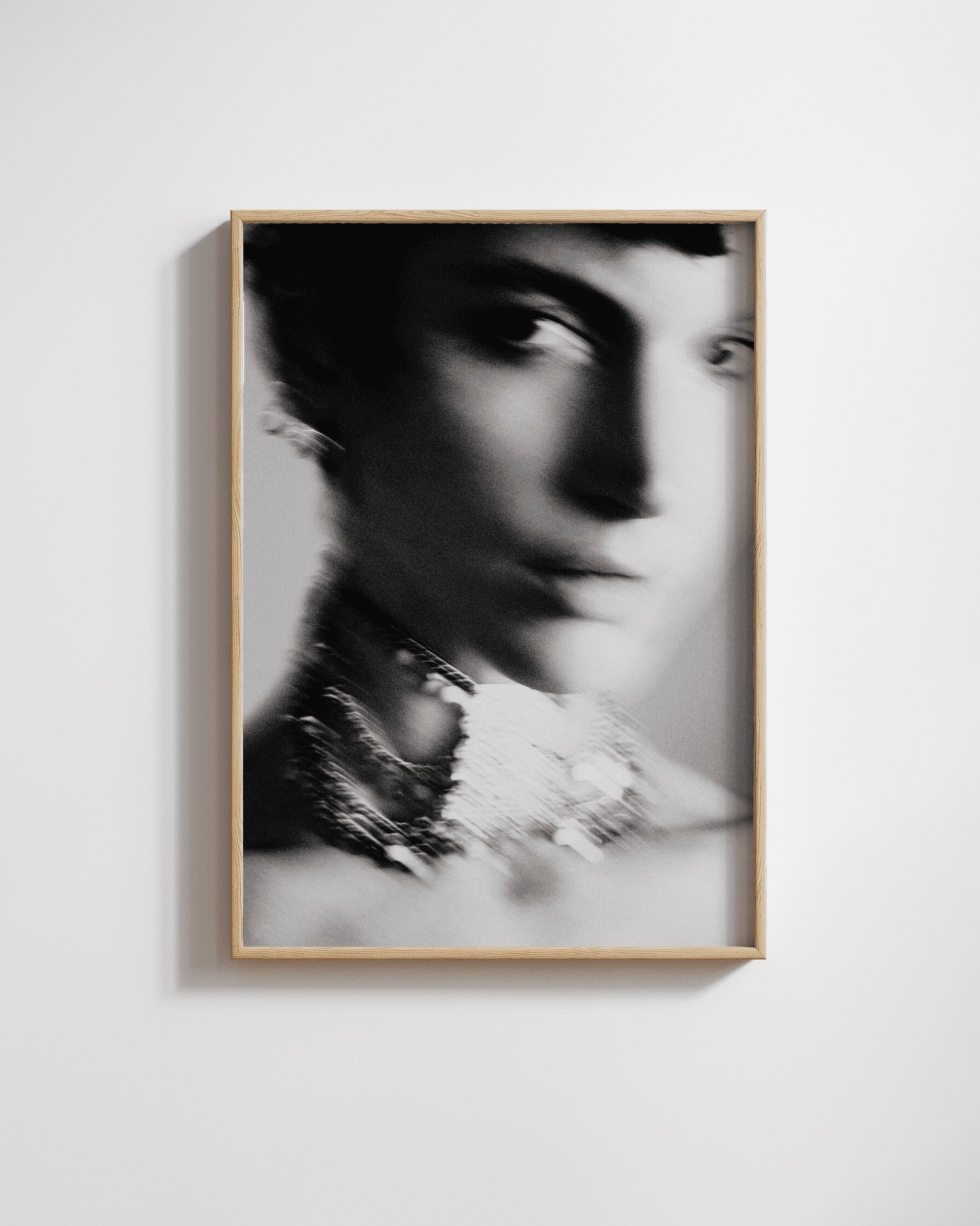 Framed black-and-white motion-blurred close-up portrait of a person's face and layered necklaces.